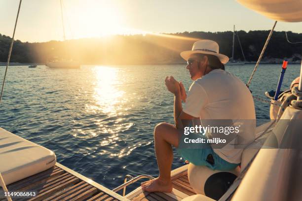 man zittend op zeilboot stern bij zonsondergang - aangemeerd stockfoto's en -beelden