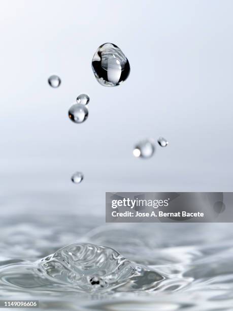 group of drops on line suspended in the air, falling down on a water surface that forms figures and abstract forms, on a white background. - bubbles white background stock pictures, royalty-free photos & images