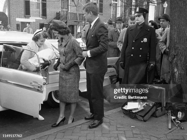 President-elect John F. Kennedy and his wife Jacqueline look on as nurse Luella Hennessey carries their infant son from the car after a short ride...