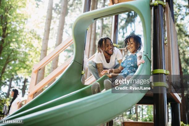 father helping his child on playground slide - tacoma stock pictures, royalty-free photos & images