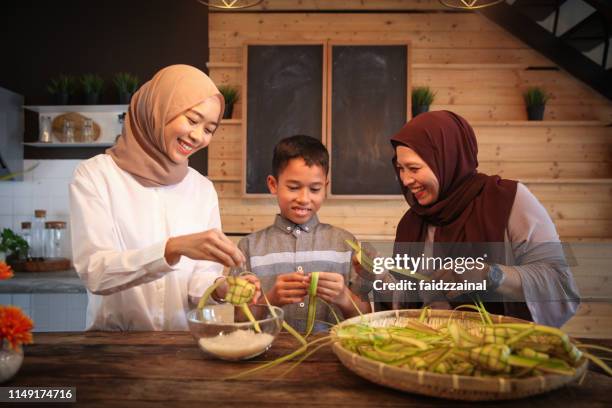 a malay muslim family of a mother and her children weaving ketupat for hari raya aidilfitri - ketupat stock pictures, royalty-free photos & images