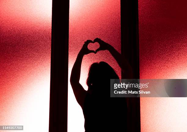 woman in silhouette making a heart shape - rear view hand window stockfoto's en -beelden