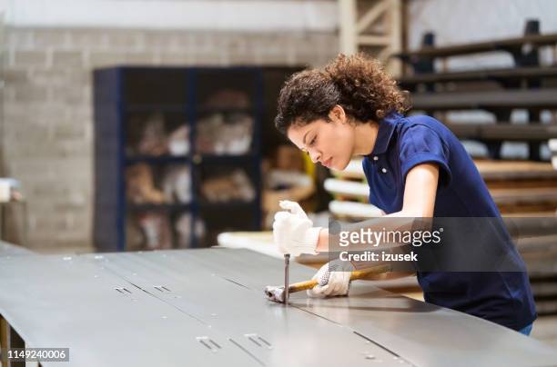 serious female engineer hammering metallic sheet - sheet metal stock pictures, royalty-free photos & images