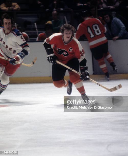 Bobby Clarke of the Philadelphia Flyers skates on the ice as Dale Rolfe of the New York Rangers follows during their game circa 1973 at the Madison...