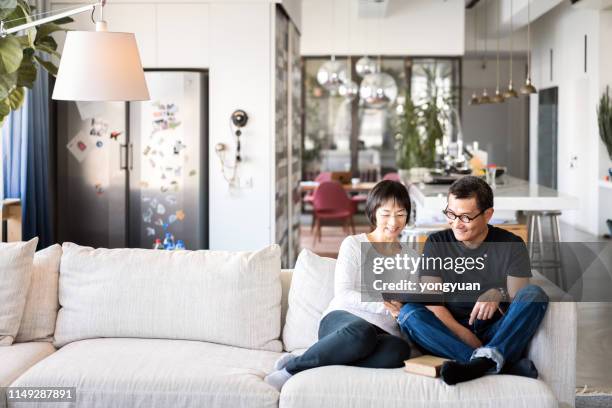 asian couple using a digital tablet on sofa - asian watching movie stock pictures, royalty-free photos & images