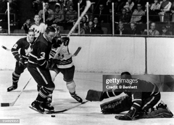 Goalie Johnny Bower of the Toronto Maple Leafs looks to cover the puck as his teammate Marcel Pronovost blocks out Orland Kurtenbach of the New York...