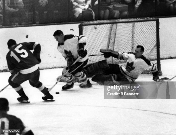 Goalie Johnny Bower of the Toronto Maple Leafs blocks the net as his teammate Tim Horton skates with the puck while being defended by Andre Pronovost...