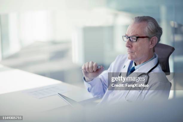 doctor zittend in office vooruitblikkend - twijfel stockfoto's en -beelden