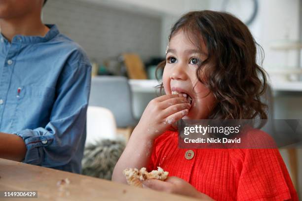 toddler girl with wavy hair enjoying cupcake with full mouth - krümel stock-fotos und bilder