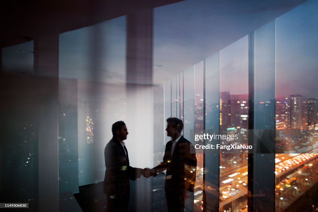 Businessmen shaking hands in office at night