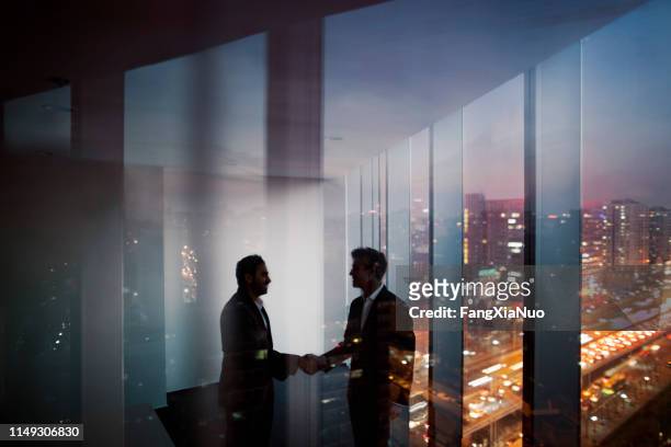 businessmen shaking hands in office at night - business agreement stock pictures, royalty-free photos & images