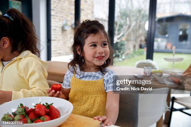 cute girl in kitchen eating strawberries from bowl - david swallow stock pictures, royalty-free photos & images