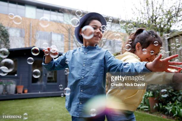 Children reaching to catch bubbles in back garden