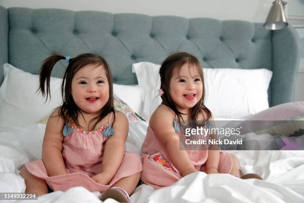 Smiling identical twin girls sitting together on bed