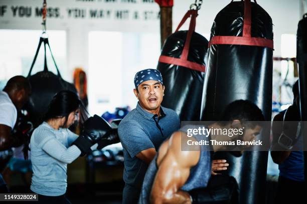 boxing trainer holding heavy bag while watching students workout in gym - filipino boxers stock pictures, royalty-free photos & images