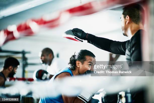 male boxer ducking during training session with trainer in boxing ring - sparring foto e immagini stock