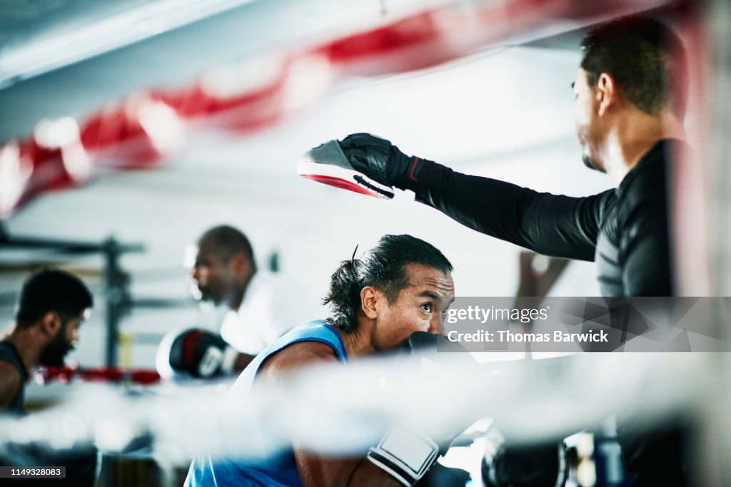 Male boxer ducking during training session with trainer in boxing ring