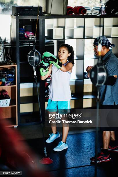 Trainer working with young female boxer on double ended bag during workout in gym