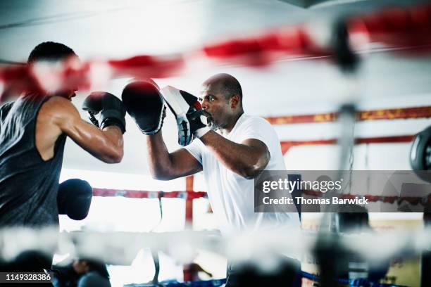 male boxer holding up punch mitts for partner while training in boxing ring - sparring stock-fotos und bilder