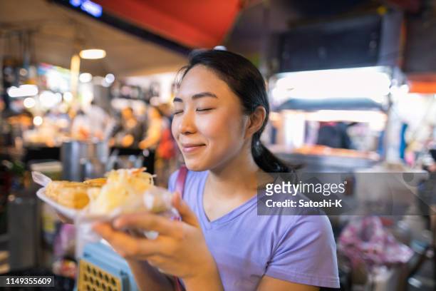 台湾ナイトマーケットの屋台で臭い豆腐を持つ幸せな若い女性 - 悪臭 ストックフォトと画像