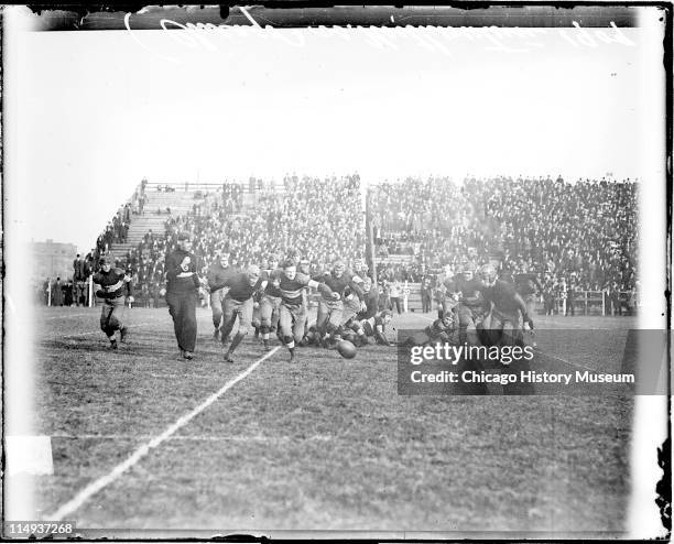 View of football players running towards a football lying on the ground during a football game between the University of Chicago and Northwestern...