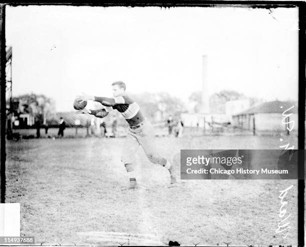 Informal full-length portrait of Northwestern University football player Ward catching a football, standing on an athletic field in or near Evanston,...