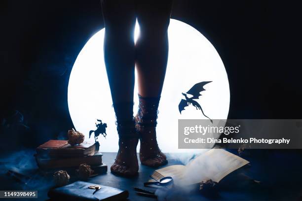 a young female writer with a fairy tale book. dragon and knight silhouettes against shiny moon background. legs in starry socks - authors night stockfoto's en -beelden