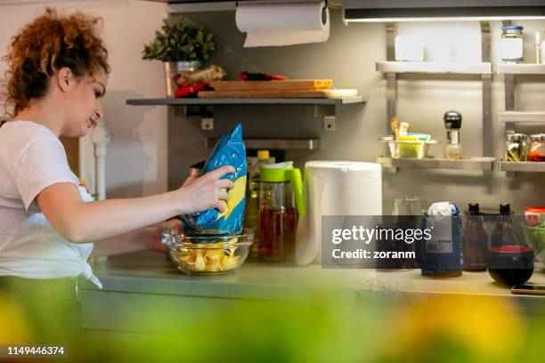 young woman pouring chips in bowl - bag of chips stock pictures, royalty-free photos & images