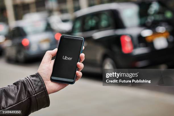 Detail of a man holding up an Honor 20 Pro smartphone with the Uber transport app visible on screen, while taxis queue in the background, on June 4,...