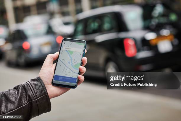 Detail of a man holding up an Honor 20 Pro smartphone with the Uber transport app visible on screen, while taxis queue in the background, on June 4,...