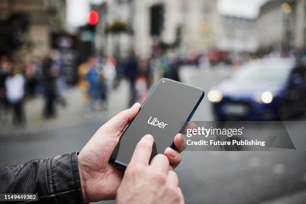 Detail of a man holding up an Honor 20 Pro smartphone with the Uber transport app visible on screen, while taxis queue in the background, on June 4,...