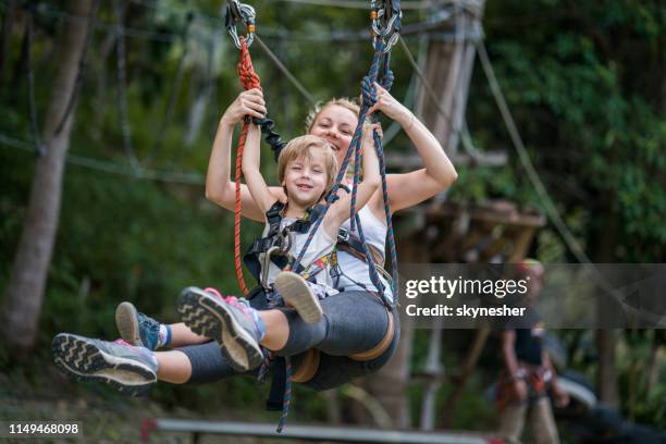 feliz madre e hijo divirtiéndose mientras tirolina en el bosque. - canopy fotografías e imágenes de stock