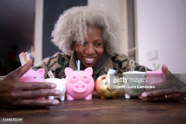 senior woman grabbing /embracing a large group of diverse piggy banks - greed stock pictures, royalty-free photos & images