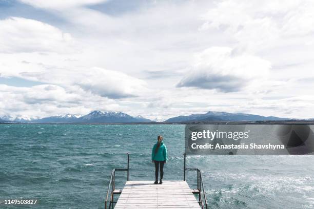 woman stays on the pier looking at the ocean and mountains in puerto natales - puerto natales stock pictures, royalty-free photos & images