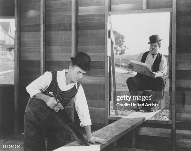 Stan Laurel saws a plank, on which Oliver Hardy is sitting, in a scene from 'The Finishing Touch', directed by Leo McCarey and Clyde Bruckman, 1928.