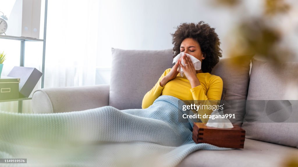 Woman blowing her nose on couch at home in the living room.