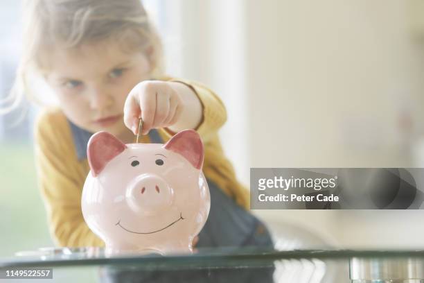 young child putting coins into piggy bank - blonde girl piggy bank stock-fotos und bilder