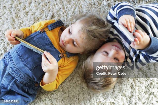brother and sister laying down looking at phones - toddler stock pictures, royalty-free photos & images
