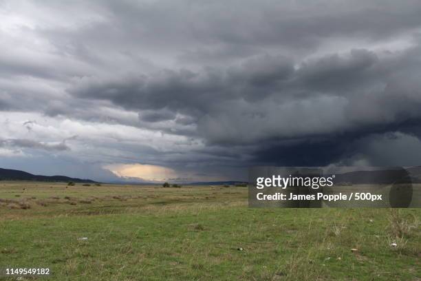 gray storm clouds over green field - james popple stock pictures, royalty-free photos & images