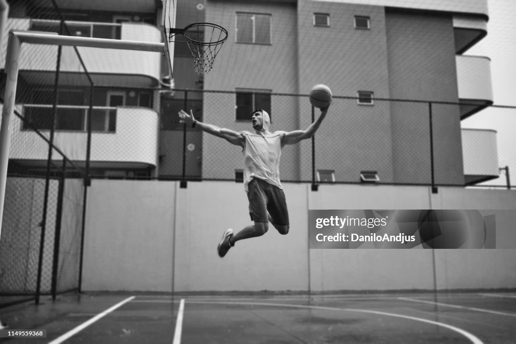 Image of an athletic young man slam dunking on a rainy day