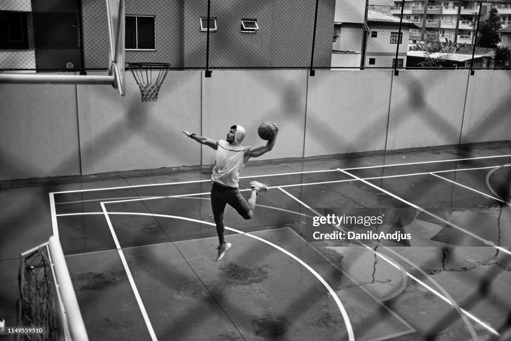 Athletic young man slam dunking on a rainy weather