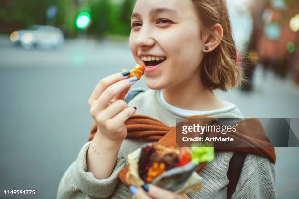 glückliches junges mädchen, das im sommer street food in der stadt genießt - snacking on the go stock-fotos und bilder