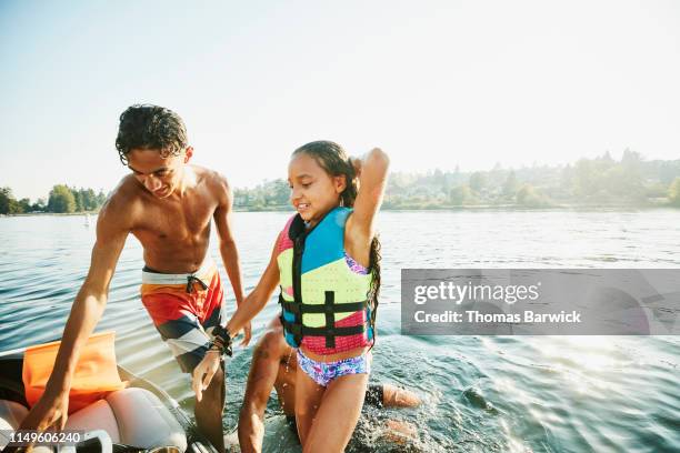 Smiling bother and sister climbing back onto boat after swimming with family in lake on summer afternoon