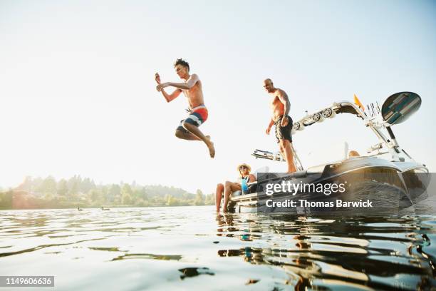 smiling parents watching son jump into lake from boat on summer evening - guy looking down stock pictures, royalty-free photos & images