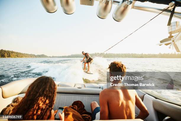 father wake surfing behind boat on summer evening while children watch - summer super 8 stockfoto's en -beelden