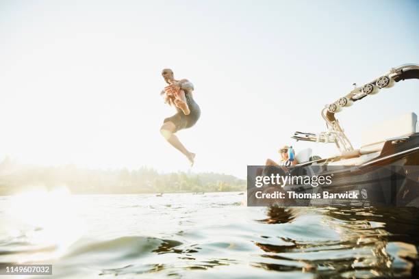 father jumping off boat into lake while family watches on summer evening - jumping of boat photos et images de collection
