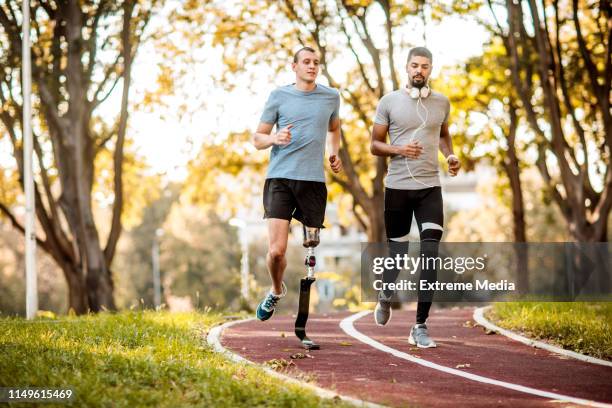 active young athlete running together with his friend with a prosthetic leg in a city park - amputee running stock pictures, royalty-free photos & images