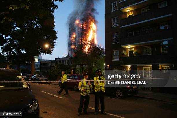 In this file photo taken on June 14, 2017 police man a security cordon as a huge fire engulfs the Grenfell Tower in west London. - Grenfell survivors...