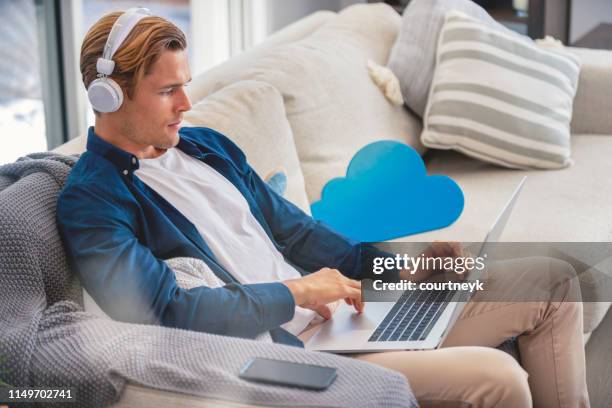 man using a laptop with cloud icon on the sofa. - electronic vapor stock pictures, royalty-free photos & images