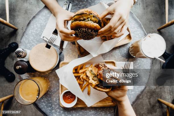 top view of friends having a good time eating burgers with french fries and drinks in a cafe - burger fries flatlay stock pictures, royalty-free photos & images